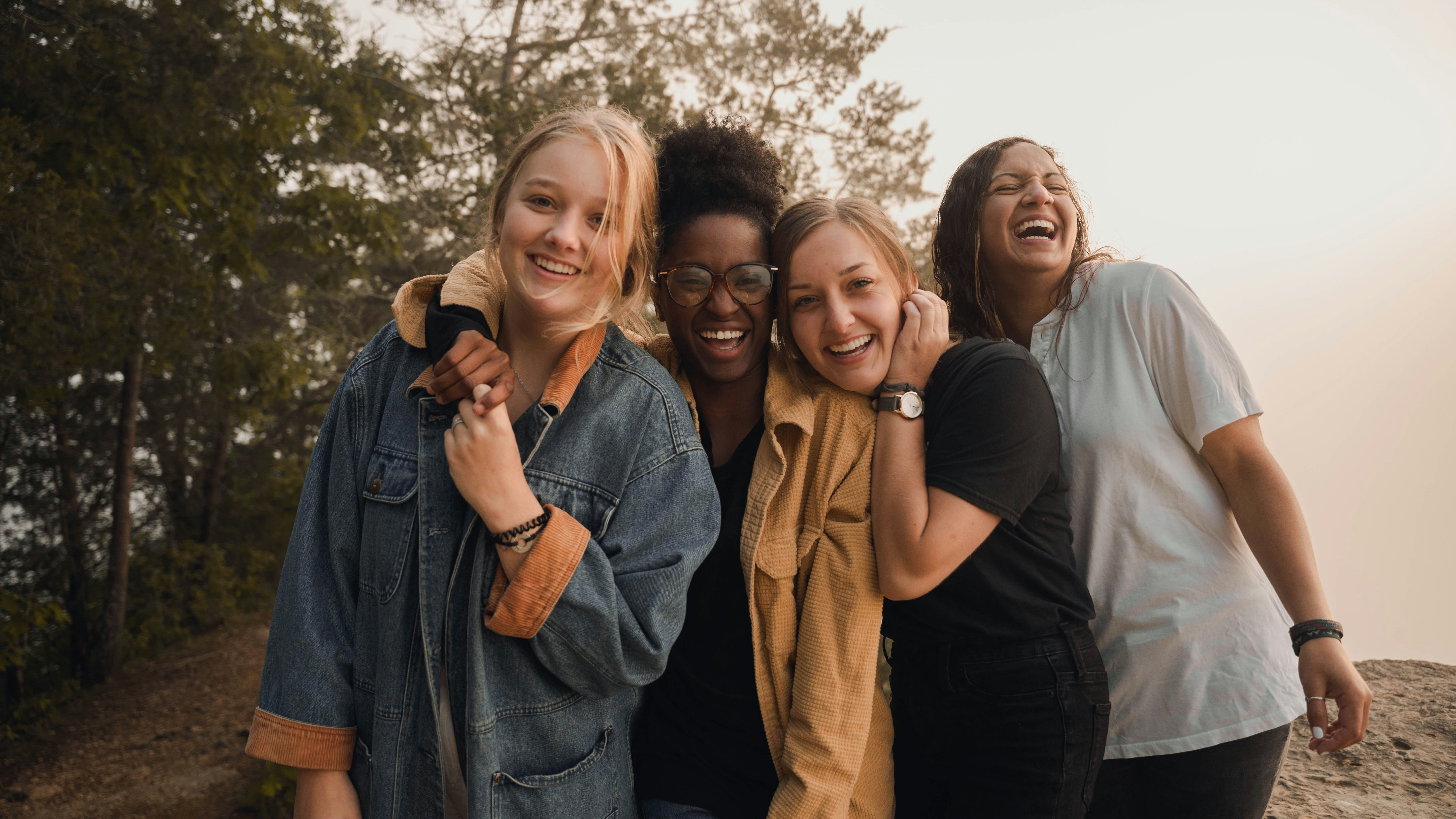Four young women laughing together outdoors with their arms around each other