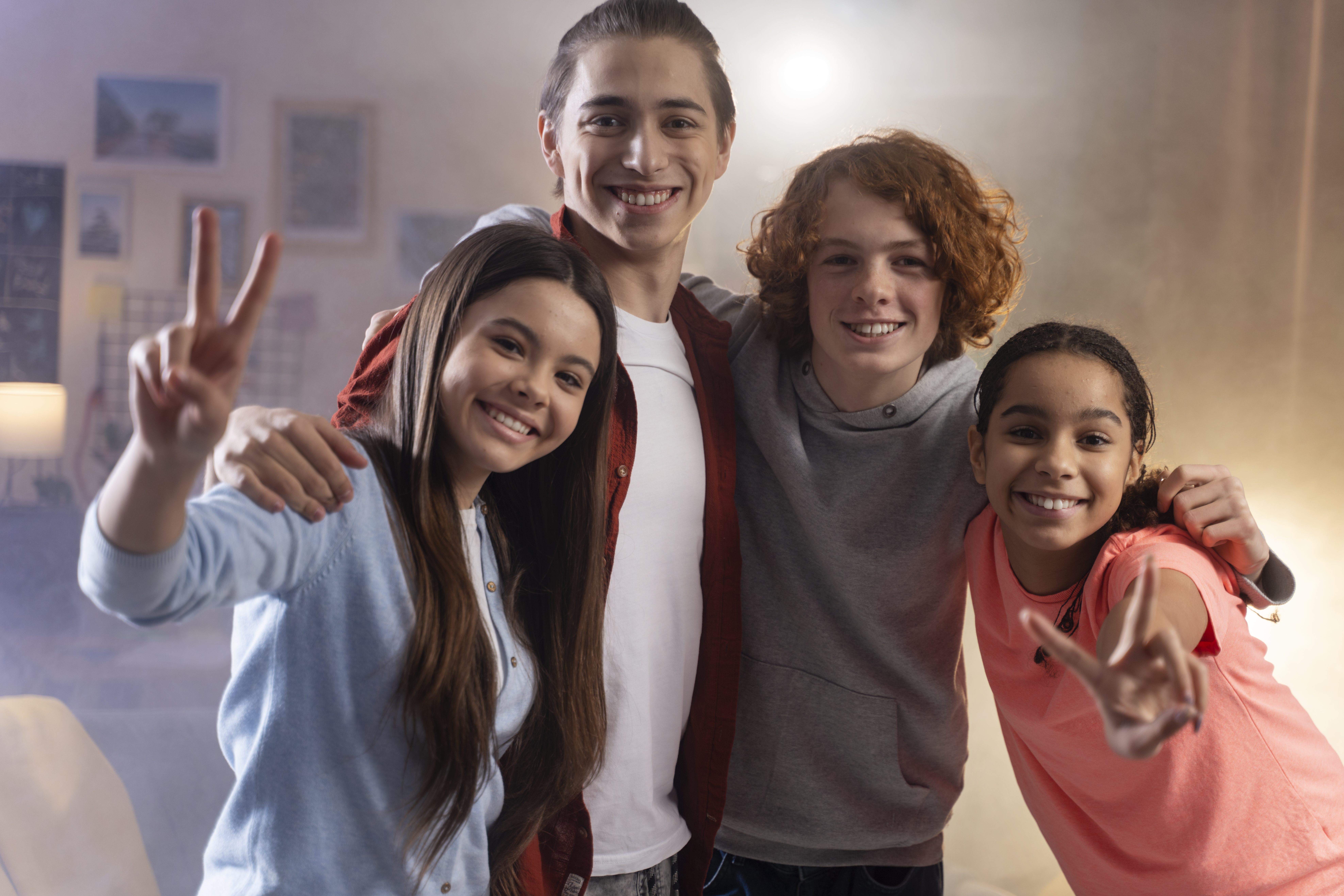 Four teenagers smiling together, two making peace signs