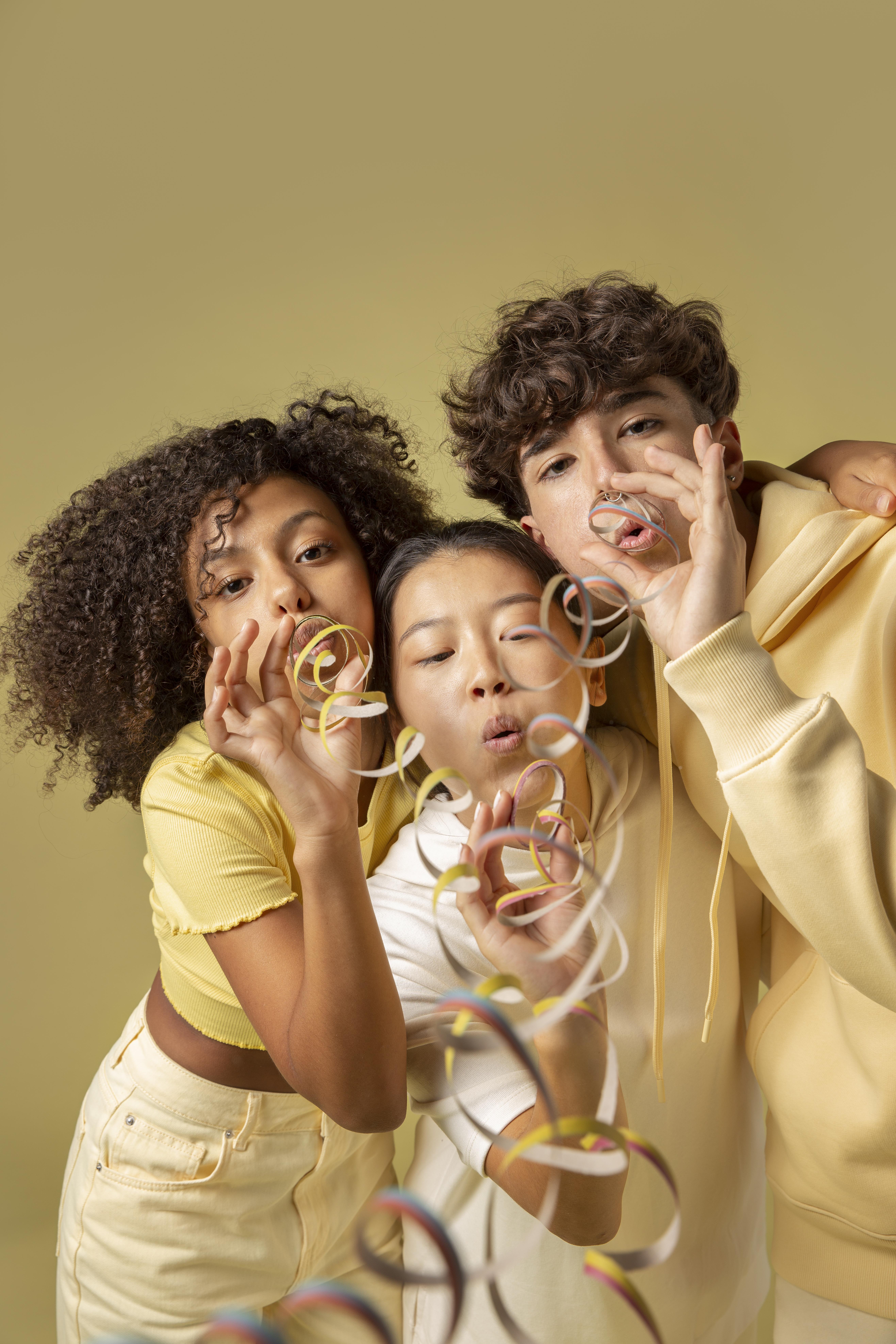 Three teenagers in yellow clothes playfully blowing party streamers